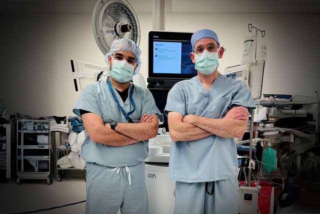 Two surgeons in scrubs and masks standing with arms crossed in an operating room.
