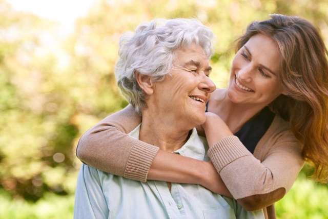 Smiling elderly woman embraced by younger woman outdoors