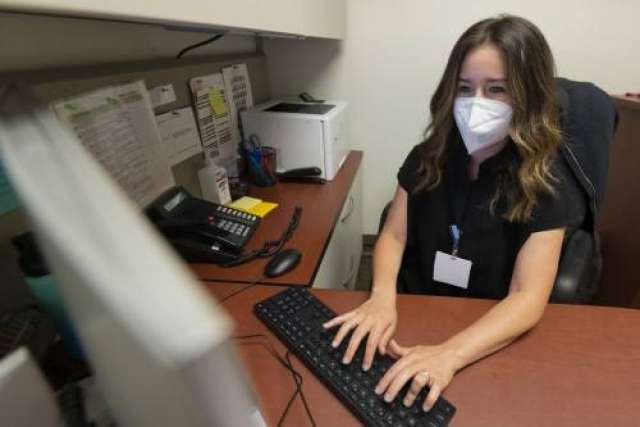 Rachel Frankenthal at a desk typing on a keyboard with monitor and phone visible