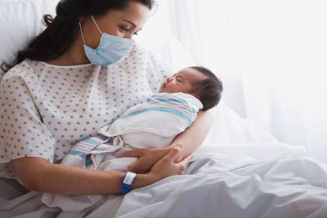 A new mother cradles her baby in a hospital bed, with natural light.