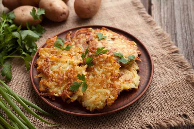 Crispy potato pancakes garnished with parsley on a wooden plate.