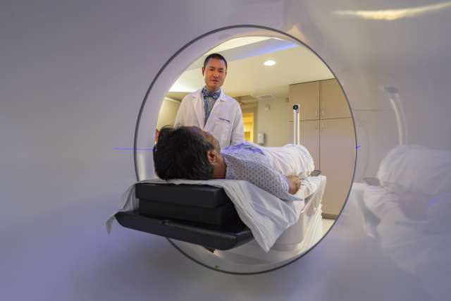 Patient on medical scanner table entering tunnel as technician stands at head.