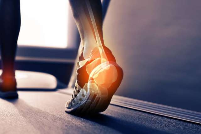 Close-up of a foot running on a treadmill, with an X-ray overlay highlighting ankle and heel bones with an orange glow, indicating pain.