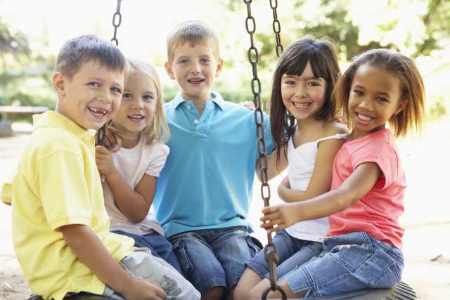 Five children sitting together on a round playground swing