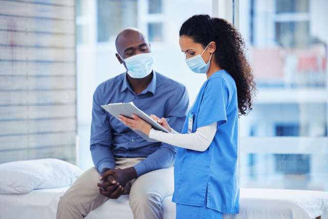 Nurse in blue scrubs showing tablet to masked male patient
