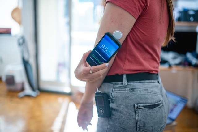 A person wearing a glucose monitor on their arm, holding a smartphone displaying data.