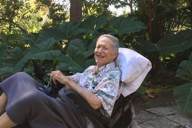 Person in wheelchair reclining outdoors amid large leafy plants