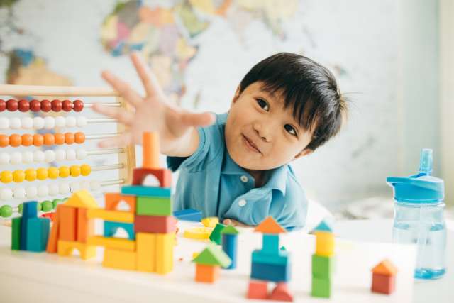 A toddler reaches his hand toward some toys on a table.
