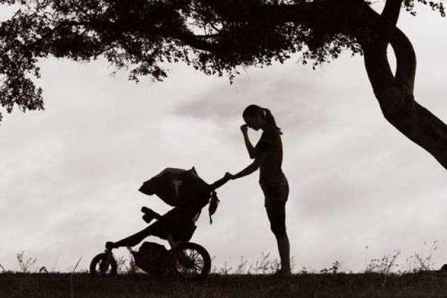 Silhouette of a woman standing beside a stroller under a tree.