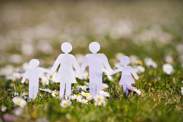 Paper cutout family of four holding hands on a grassy field with daisies