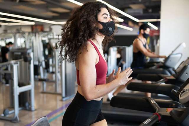 Woman running on treadmill in gym wearing a face mask