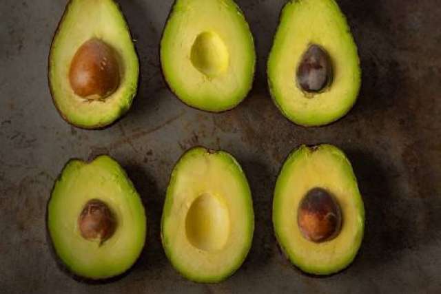 Six avocado halves on dark background, three with pits
