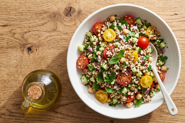 Grain salad with halved cherry tomatoes, herbs and a spoon; olive oil bottle beside.