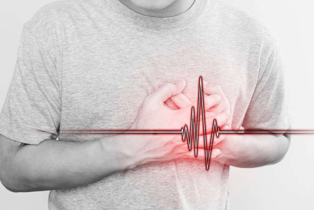Person wearing a gray t-shirt clutching chest with both hands, overlaid with a red heartbeat line graphic indicating heart-related distress.