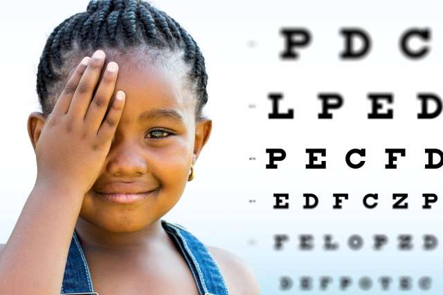 A child blocking their face with a hand in front of an eye chart.