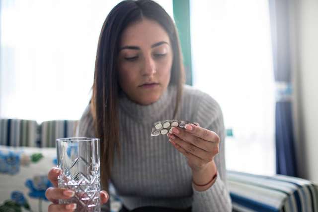 Woman examining pills while holding a glass of water