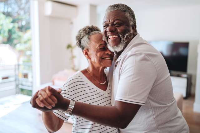 Smiling older couple embracing in a sunlit living room.