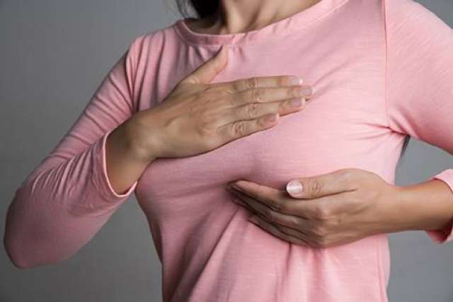 Person wearing a pink long-sleeve shirt performing a breast self-exam by placing one hand on the chest and the other under the breast.