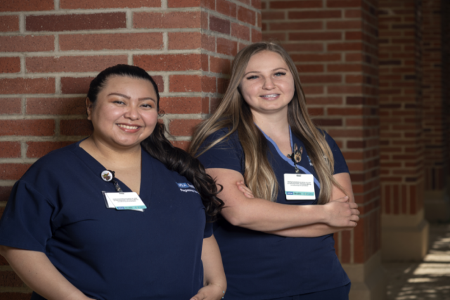 Kennedy Davis, left, and Dahlia Maldonado, right, leaning against a brick pillar, smiling and looking at the camera.