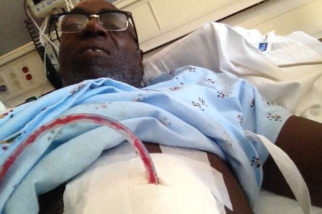 Person in hospital gown reclining with tube and bandage on abdomen