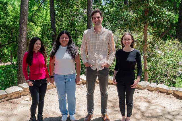 Four people standing side by side on a wooded path