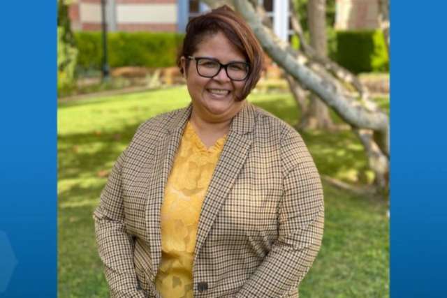 Diana Ramirez, a Black woman with short, styled hair, stands outside, smiling and wearing a mustard yellow top and a tan cardigan.