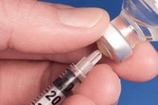 Close-up of a hand drawing liquid from a vial into a syringe.