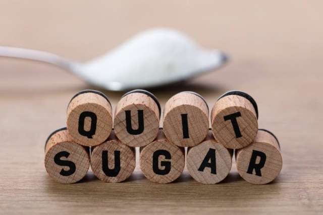 Wooden blocks spell "QUIT SUGAR" with a spoonful of sugar in the background.