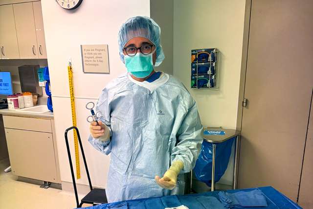 A healthcare professional in scrubs and a mask stands by a medical table with supplies.