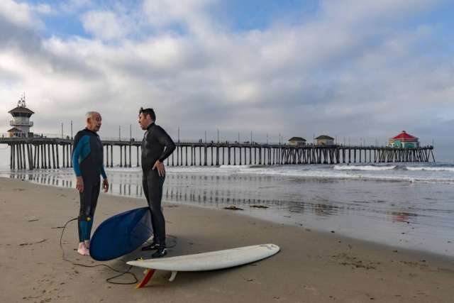 Dr. Sassoon and Robert Lombard  having a conversation on the shore beside their surfboards
