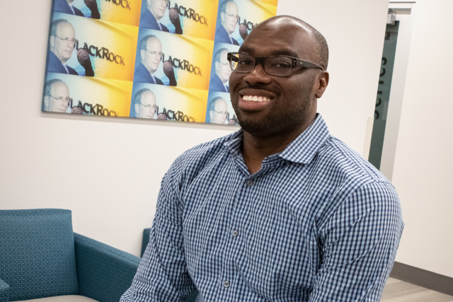 Dr. Obi Emeruwa, Assistant Clinical Professor at UCLA, smiles in a blue checkered shirt, seated in a modern office.