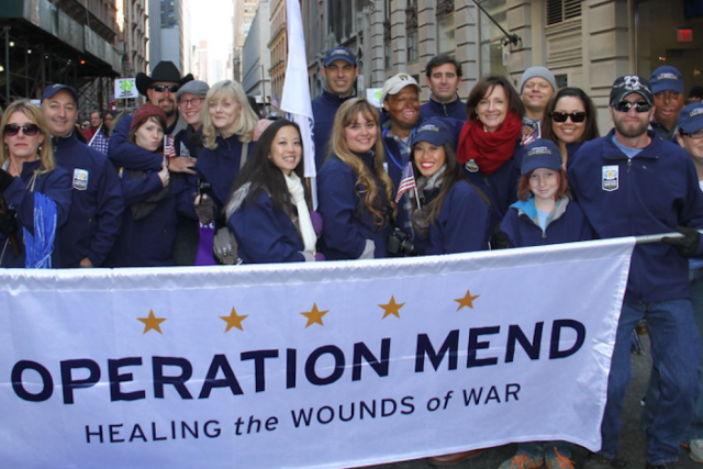 Group of Operation Mend participants and staff holding a banner reading “Healing the Wounds of War” during a UCLA Health event.