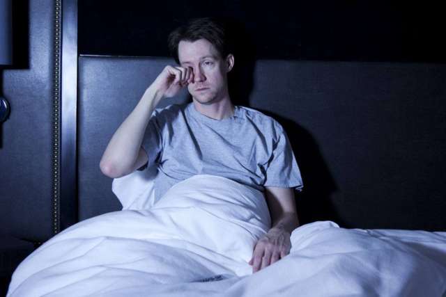 Man sitting up in bed rubbing his eye
