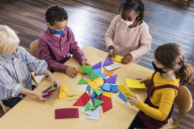 Four children engaged in a hands-on activity with colorful paper pieces on a table.