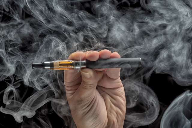 Hand holding an electronic cigarette over a dark background