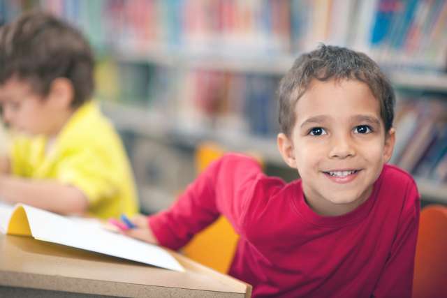 A young smiling boy sits at a school desk.