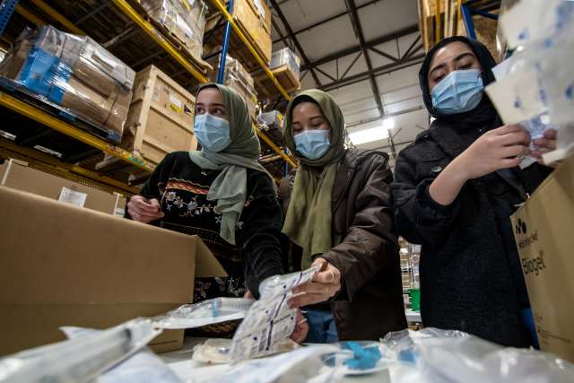 Three women in hijab packing items in boxes in a warehouse