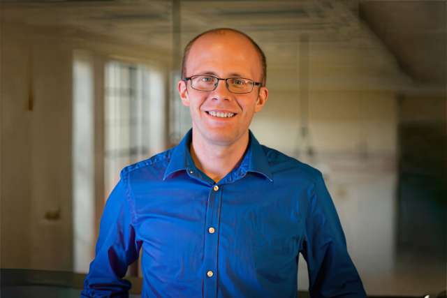 Michael Birnbaum smiling, wearing a blue shirt and glasses, office background
