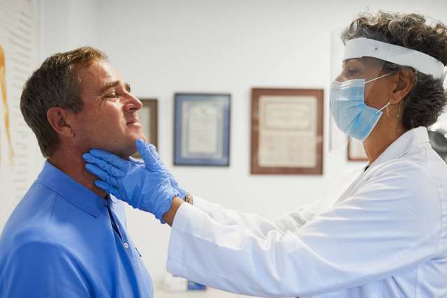 Doctor in mask palpating male patient's neck exam