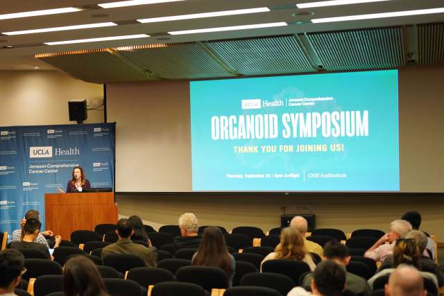 Speaker at podium addressing seated audience at Organoid Symposium