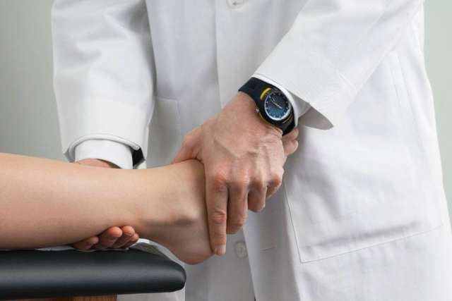 Healthcare professional in a white coat examining a patient’s ankle and foot during a physical assessment.