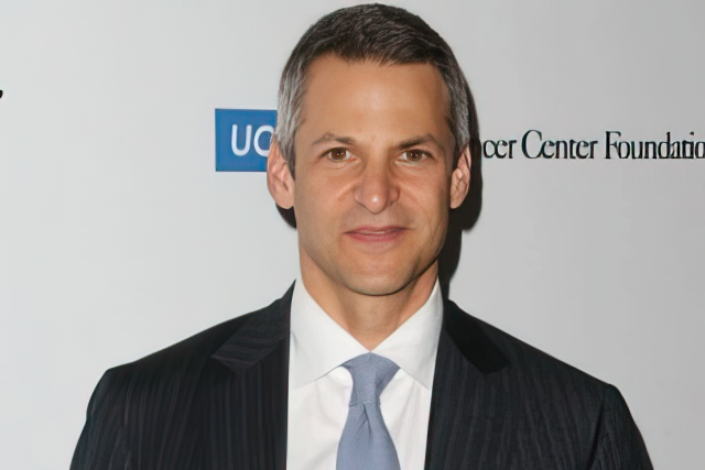 Joe Cohen, holding an award, wearing a suit and tie, at the Taste For a Cure 2013.