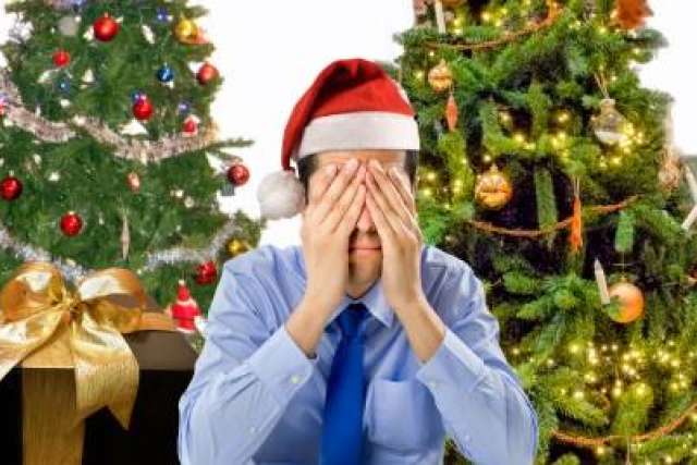 Man in a Santa hat covering his face, surrounded by decorated Christmas trees.