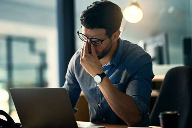 Man in glasses at laptop rubbing his eyes