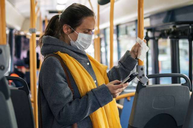 A woman with a yellow scarf checks her phone on a bus.