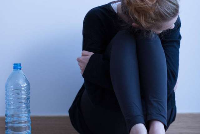 Person seated on floor hugging knees beside plastic water bottle