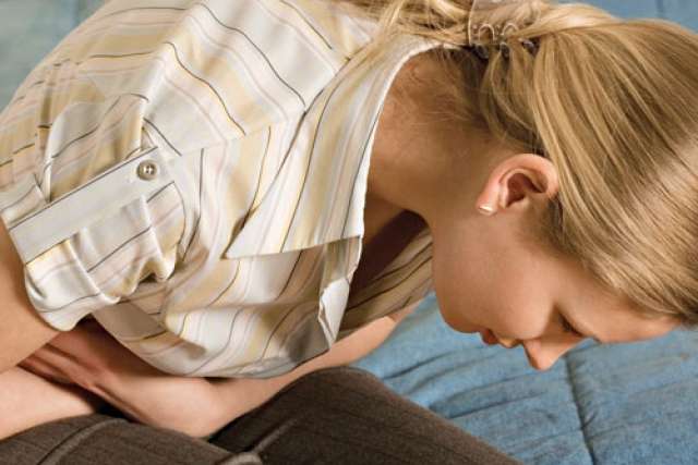 Person sitting on a couch, hunched over with discomfort, wearing a striped shirt.