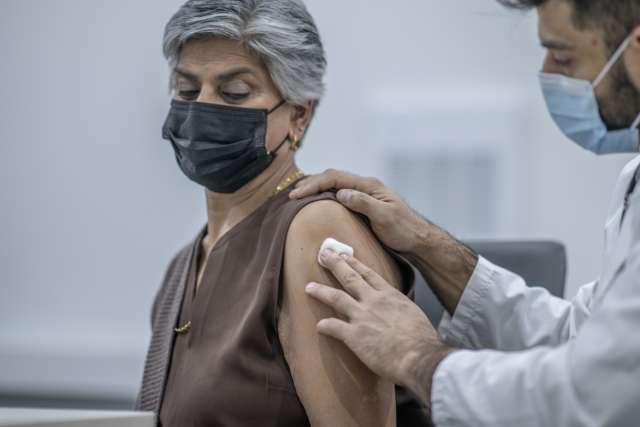 A woman visits the doctor and receives an injection. She and her doctor are both wearing protective masks