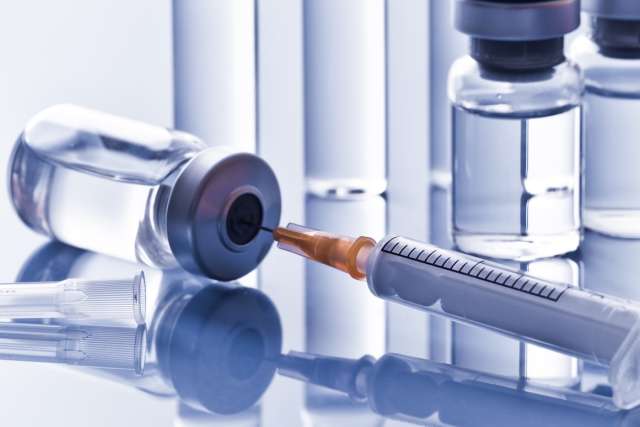 Syringe with needle beside medical vials on reflective surface.