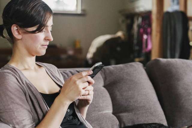 Person relaxing on a couch while looking at a smartphone, with soft lighting and a lived‑in home interior in the background.